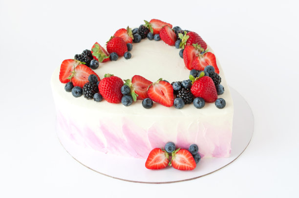 情人节心形蛋糕，上面有粉红色的奶油，以草莓、蓝莓和黑莓装饰，白色的背景。图片下载