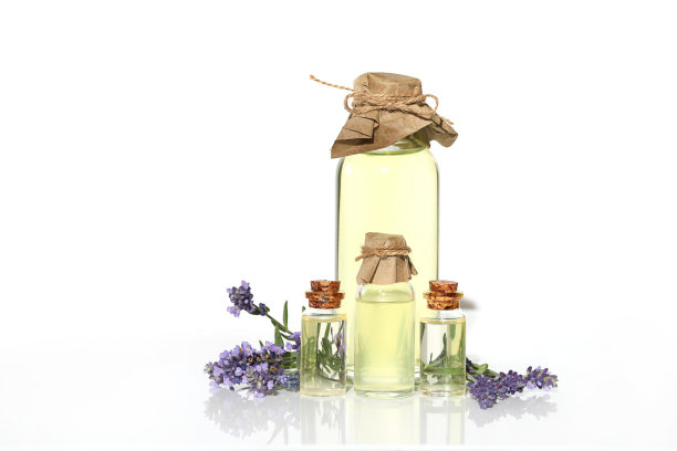 薰衣草油。四个装有薰衣草油的透明玻璃瓶，薰衣草花在白色的背景上。植物美容图片下载