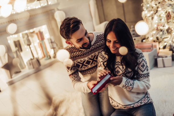 美丽的情侣在家里美丽的圣诞树旁一起等待新年。图片下载