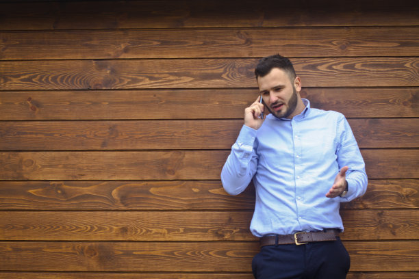 一个英俊男子的肖像在一个木制的墙壁背景衬衫。商人，穿着时髦的老板。性感的男人在打电话。库存图片设计图片下载