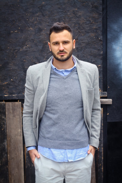 一个穿着时髦的人靠在一堵蓝色的墙上。冬天寒冷，秋天天气。一个变暖的人。设计素材照片图片下载