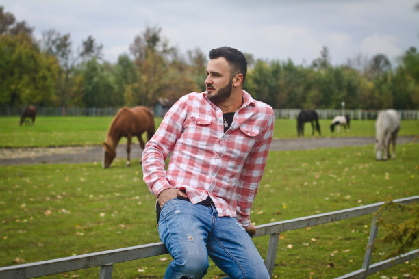 年轻英俊的牛仔。一个男人在他的篱笆附近的农场里当农民。农村景观,乡村。树木、字段农场。股票的照片图片下载