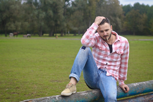 年轻英俊的牛仔。一位男性农夫正坐在他农场的篱笆上。农村景观,乡村。树木、字段农场。设计图片图片下载