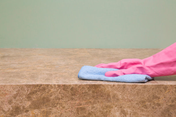 员工手拿橡胶防护手套，用超细纤维布擦拭大理石桌子表面的灰尘。早春定期大扫除。商业清洁公司理念。图片下载