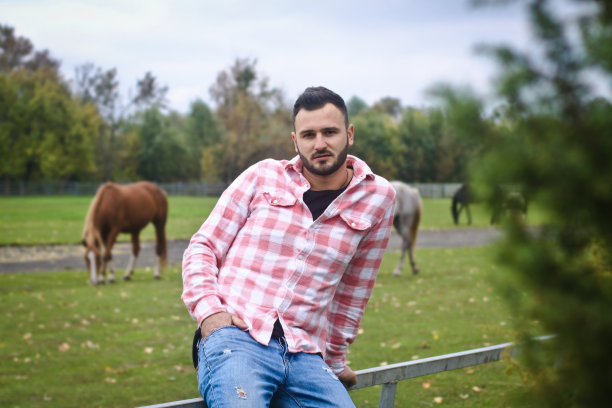 年轻英俊的牛仔。一个男人在他的篱笆附近的农场里当农民。农村景观,乡村。树木、字段农场。股票的照片图片下载