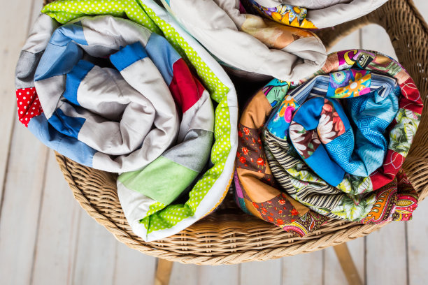 拼接和时尚概念——特写三种颜色的棉被卷成一个管，放在一个柳条椅子上，库存成品在一个白色的背景，俯视图图片下载