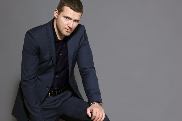 一个穿着蓝色西装的男人正坐在一个灰色背景的演播室里图片下载