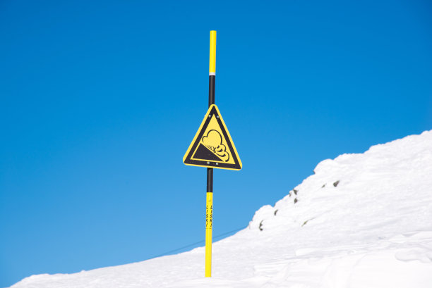 滑雪胜地的雪崩危险标志。有关滑坡和无越野滑雪的信息。蓝色天空背景上的黄色三角形。俄罗斯,Khibiny山脉。图片下载