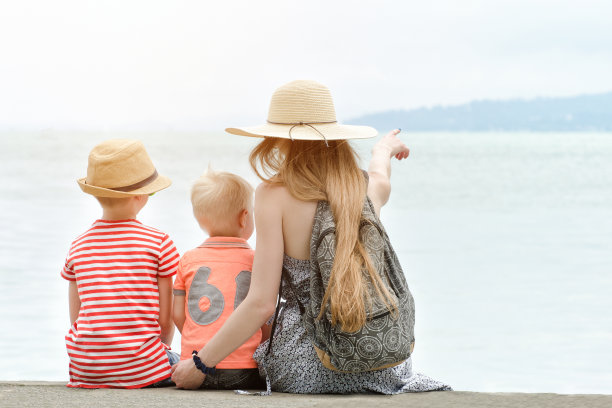 妈妈和两个儿子坐在码头上，欣赏着远处的海和山。后视图图片下载
