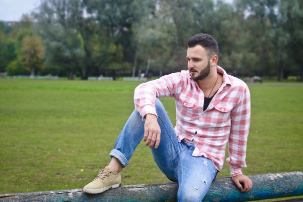 年轻英俊的牛仔。一位男性农夫正坐在他农场的篱笆上。农村景观,乡村。树木、字段农场。设计图片图片下载