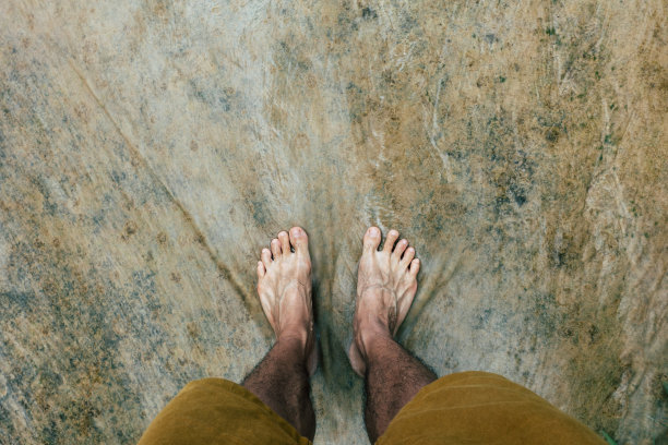 男人的脚踩在瀑布旁边的岩石上图片下载