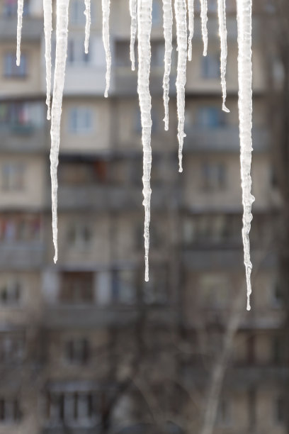 危险的冰柱悬挂在满是积雪的屋顶上。冬季小镇的街道上有巨大的冰柱图片下载