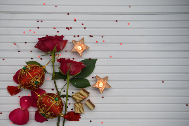 浪漫的圣诞美食照片，红玫瑰蜡烛和豪华巧克力都撒上了红心，白色的木头背景有空间图片下载