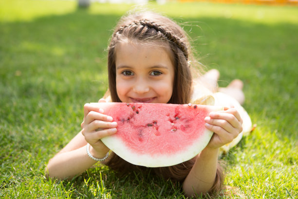 快乐可爱的小女孩躺在草地上吃西瓜在夏天的时间。快乐的小女孩在户外玩夏天。图片下载