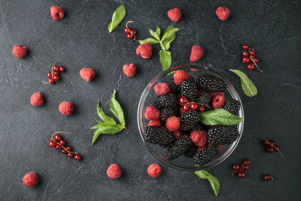俯视图照片在一个玻璃盘子与成熟的红色黑莓，覆盆子，醋栗和绿色薄荷叶在一个黑色的表面。图片下载