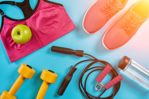 运动员套装，女性服装，哑铃和水瓶在亮蓝色的背景。太阳耀斑图片下载