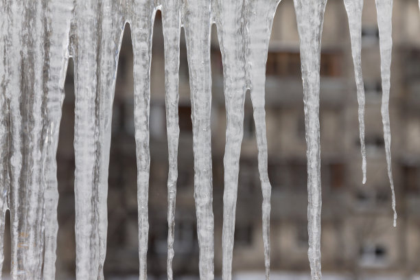 危险的冰柱悬挂在满是积雪的屋顶上。冬季小镇的街道上有巨大的冰柱图片下载