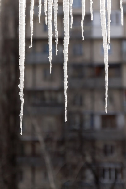 危险的冰柱悬挂在满是积雪的屋顶上。冬季小镇的街道上有巨大的冰柱图片下载
