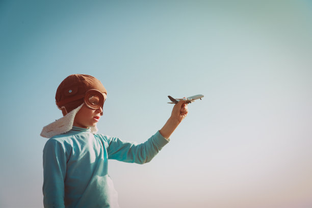 戴着头盔和眼镜的小男孩在空中玩玩具飞机图片下载
