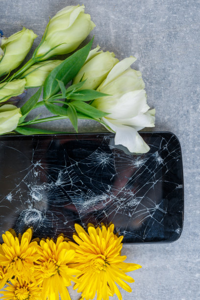 一个坏掉的手机横卧在石头背景上的鲜花之间图片下载