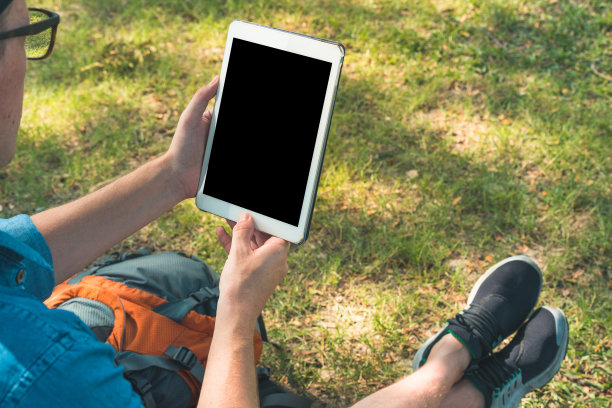 一个背着背包拿着平板电脑的人在大自然中。数字生活的概念图片下载
