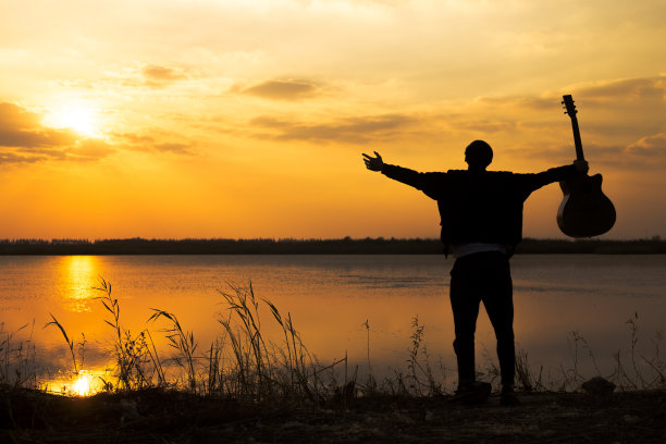 夕阳下，挎着吉他的男人的剪影图片下载
