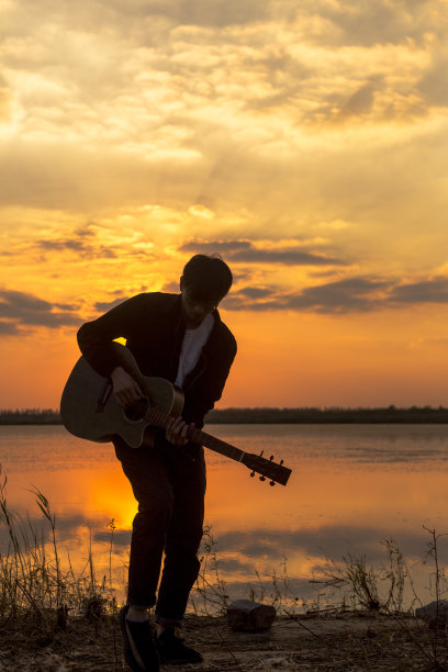 夕阳下，挎着吉他的男人的剪影图片下载