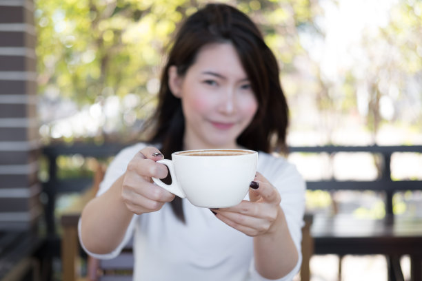 年轻女子拿着一杯咖啡，微笑着在早晨。选择性专注于咖啡杯图片下载