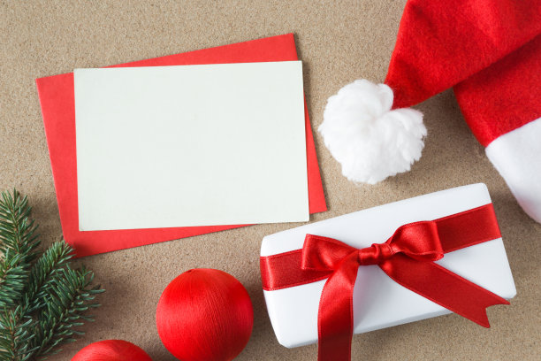 白色空白贺卡与圣诞老人红帽子和白色礼盒与丝带在炎热的热带沙滩上。圣诞节和新年的概念。文本的空位置。素材图片
