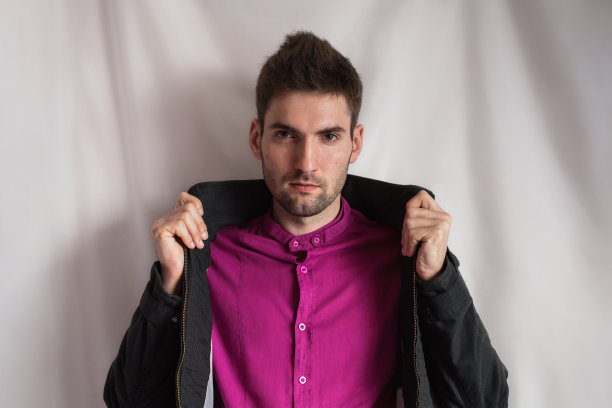 正面肖像中一位留着胡子的英俊青年身穿紫色衬衫和黑色夹克，双手放在白色背景上，竖着拍照，望着相机图片下载