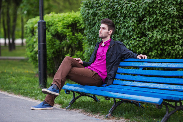 他是一个年轻英俊的男子，留着黑头发和胡子，穿着衬衫和黑夹克走在街上。男性的街头风格。大自然在春天。在城市里散步。图片下载