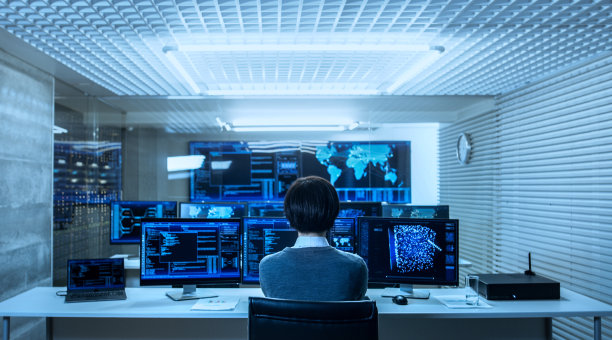 IT工程师与显示图形的多显示器，功能神经网络一起工作的后视图。他在一个技术先进的系统控制数据中心工作。图片下载