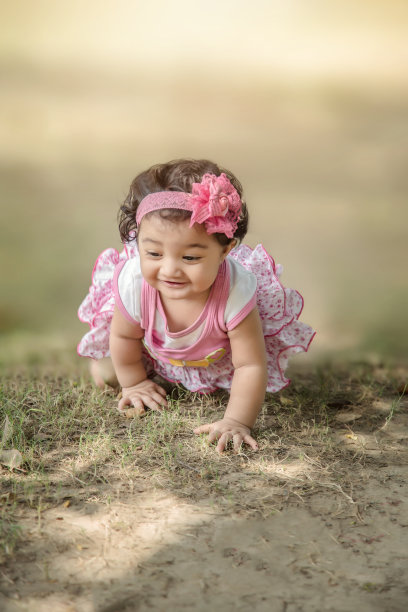 6个月的快乐印度/亚洲小孩穿着粉红色的衣服在草地上爬行和玩耍。景深浅。图片下载