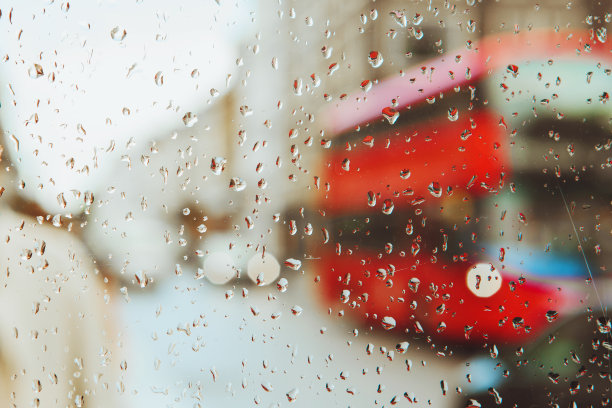 雨滴落在玻璃上，红色的伦敦公交车灯光模糊了背景。图片下载