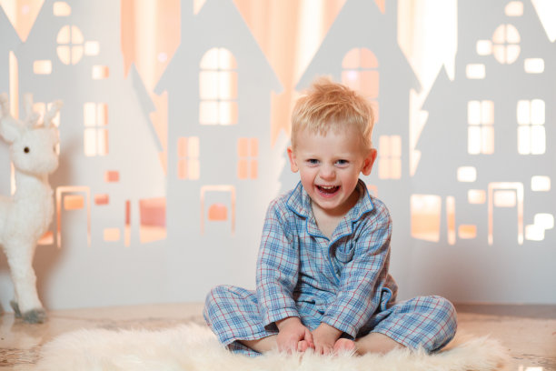 可爱的金发小男孩穿着睡衣在圣诞玩具纸房子附近图片下载
