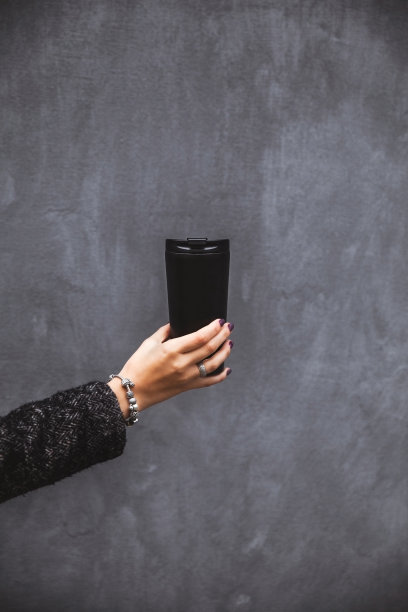 有着美丽美甲手的女孩在灰色背景下拿着一个黑色的真空玻璃杯图片下载