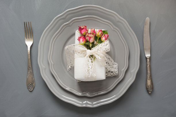 喜庆的餐桌摆设，女性用玫瑰作为礼物，复古的餐具，银器和装饰品用灰色。前视图。的概念。图片下载