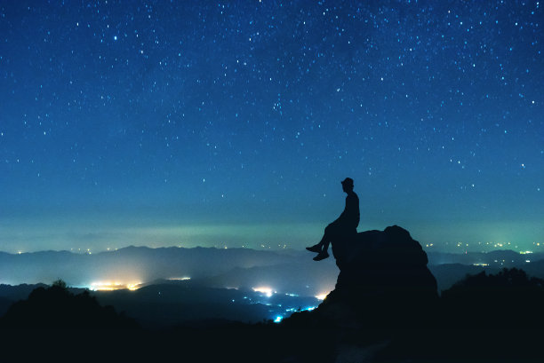 男人坐在夜空背景的大石头上素材图片