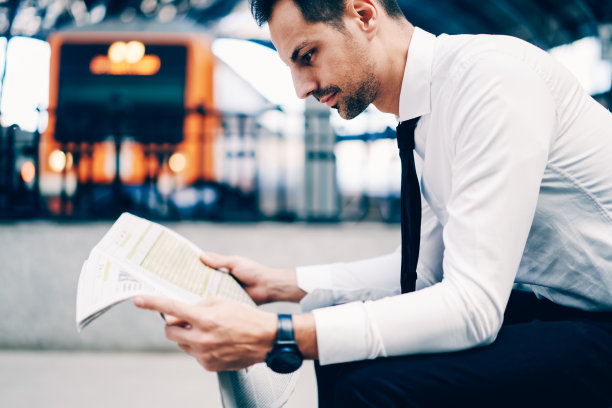 成功律师身着时尚正装在晨报财经专栏阅读最新新闻的裁剪图像。银行的侧视图与手表搜索信息在大众媒体素材图片