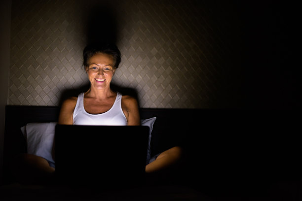 快乐成熟的女人晚上在床上用笔记本电脑图片下载