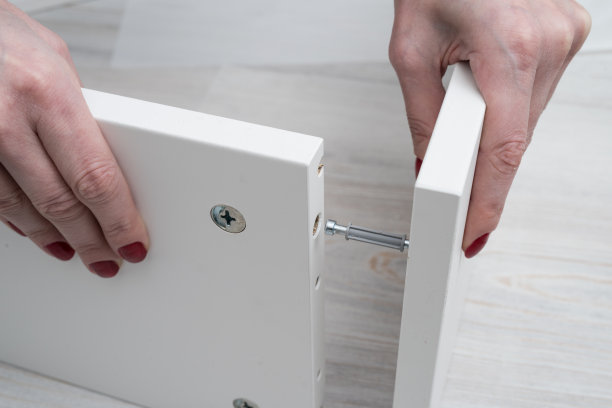 该女子将该部件以拆装的形式插入在商店购买的储物柜的白色家具面板中。连接两个垂直位置的墙的过程。图片下载