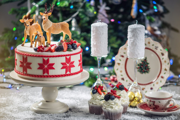 白色圣诞蛋糕与红色装饰顶部装饰乳香鹿和新鲜的浆果在节日的桌子上图片下载
