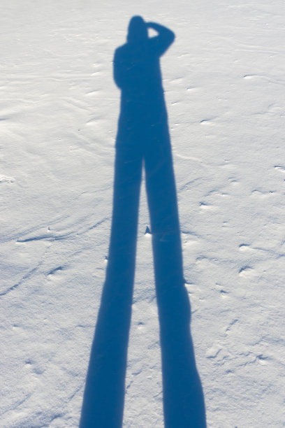 夕阳的余晖投射在雪地上的成年男性的影子图片下载