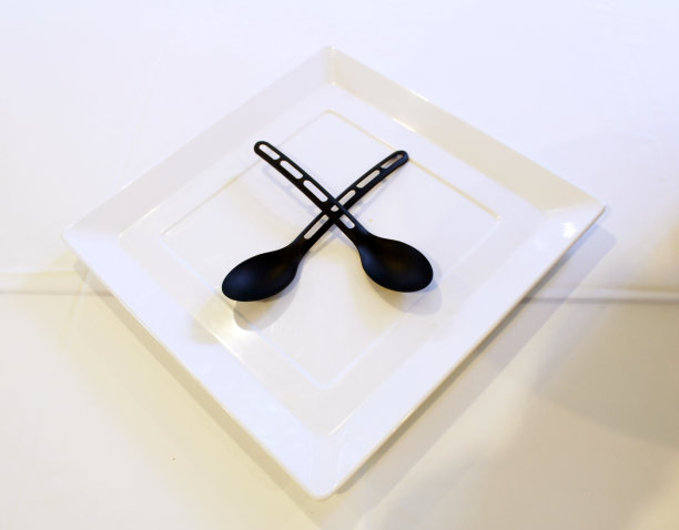 一对黑色的勺子放在一个白色的方形餐盘在餐桌上。图片下载
