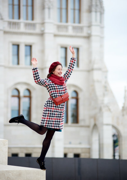 快乐的女游客站在台阶的边缘，另一条腿和双手举起。背景模糊的布达佩斯古建筑。快乐翱翔的女孩图片下载