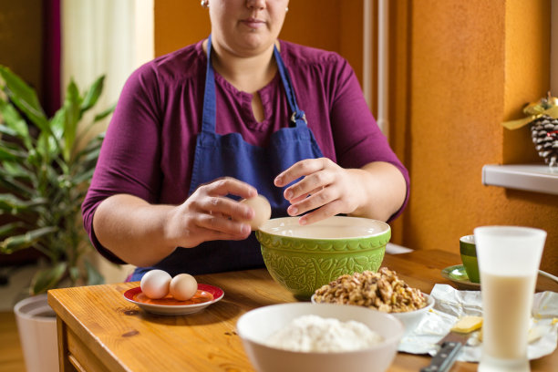近距离的照片，年轻女性的手打破了一个鸡蛋边缘的绿色碗，碗里装满了核桃放在旁边，烘焙的原料都放在桌子上图片下载