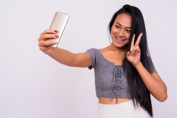 年轻美丽的亚洲女人的肖像使用手机的白色背景图片下载