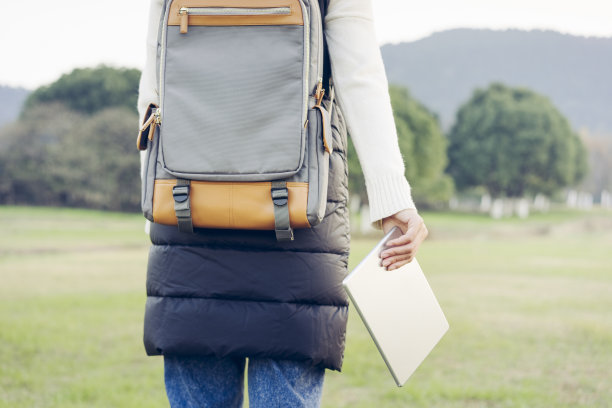 年轻女性背着平板电脑背包走在草坪上图片下载