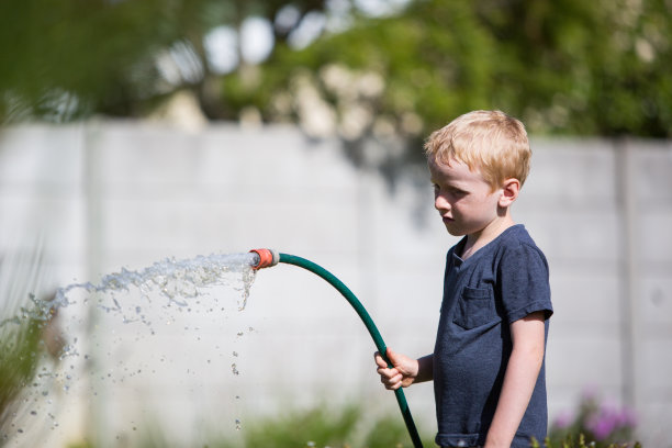 男孩用水管给花园浇水图片下载