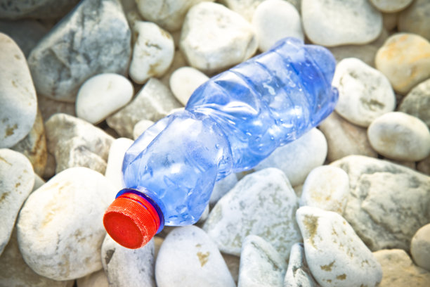 沙砾海滩上的红色瓶盖蓝色空塑料瓶图片下载